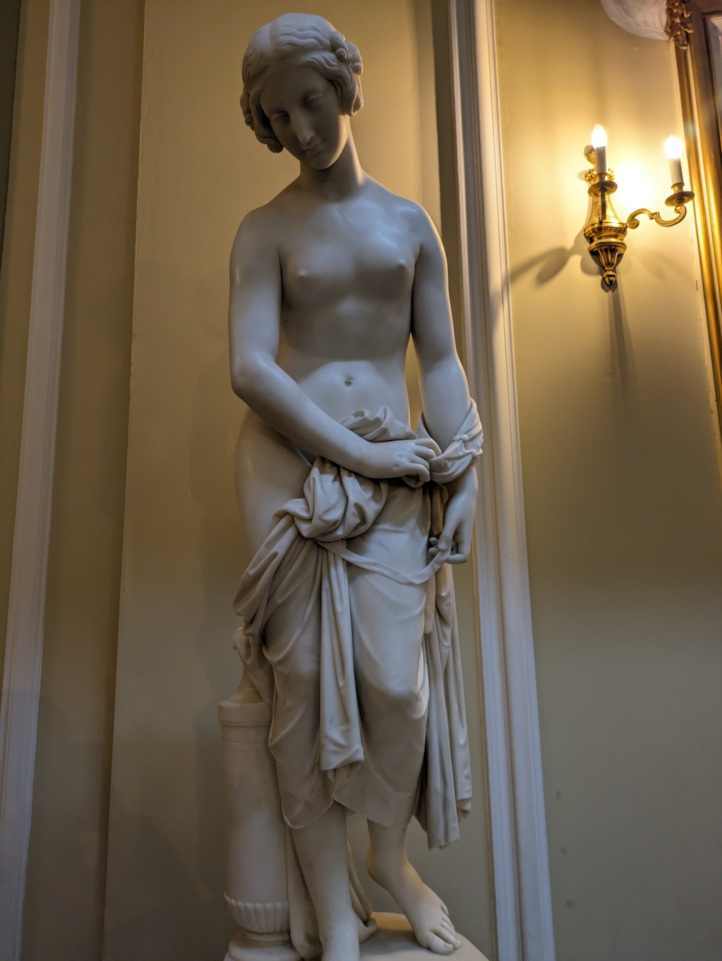 Statue of a semi-nude women with cloth hanged over her lower-half with top-half and breasts uncovered.
