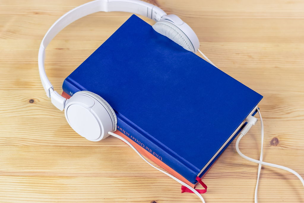 Headphones places over a blue and a red book, &ldquo;plugged in&rdquo; at bottom of the blue book.