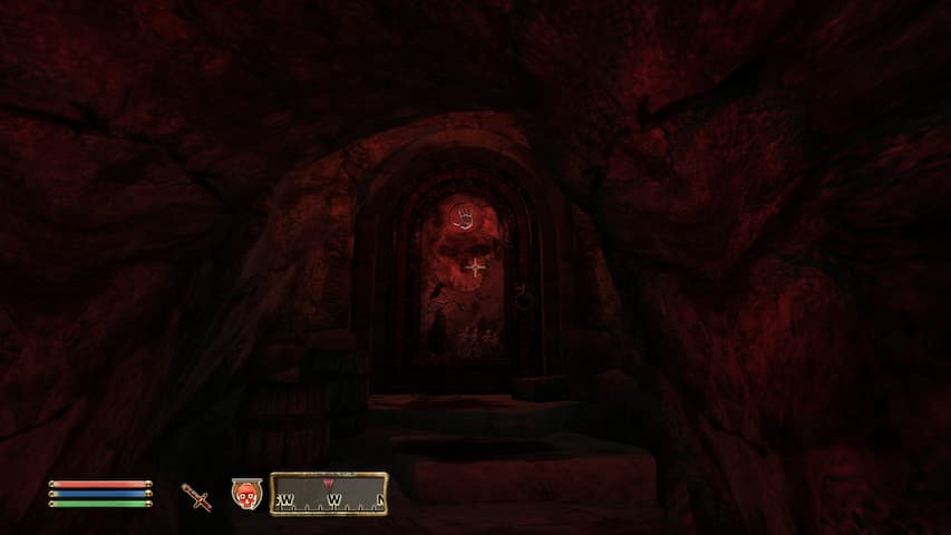 A door with a skull curned into it, located in within a tunnel with blood-soacked steps leading to the door, lit by red lighting.